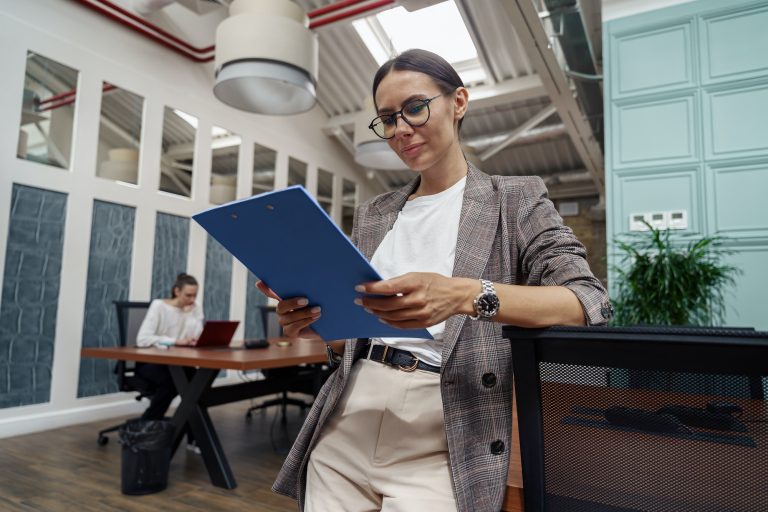 Portrait of smiling businesswoman with documents standing in modern office